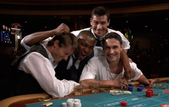 Four men sat in casino playing roulette while having fun and looking happy.