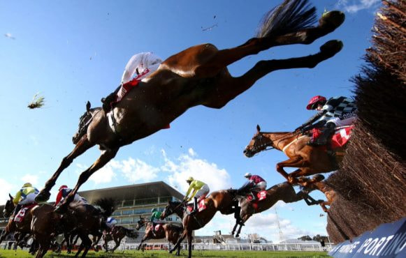 Horses clearing a chase obstacle at Newbury Racecourse.