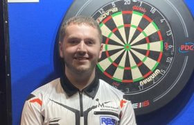 Teenaged Darts star Leighton Bennett posing before a dart board