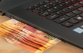 Stack of Money Next to a Laptop