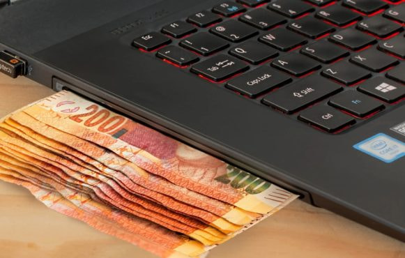 Stack of Money Next to a Laptop