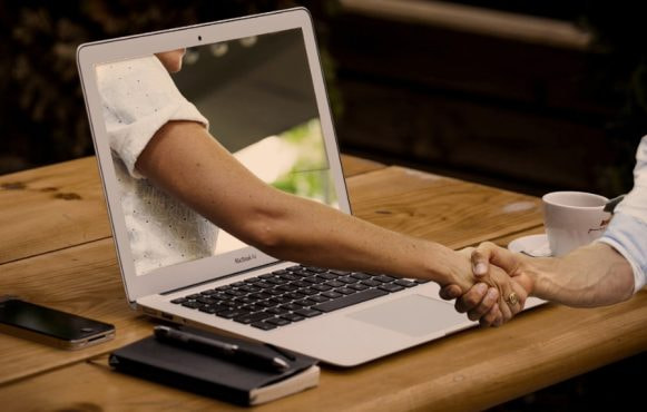 En mansarm sticker ut ur en datorskärm och skakar hand med person framför datorn.