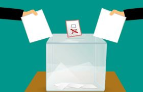 Två händer som lägger ner röster i en låda