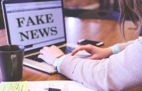 Person skriver på laptop med texten “Fake News”.