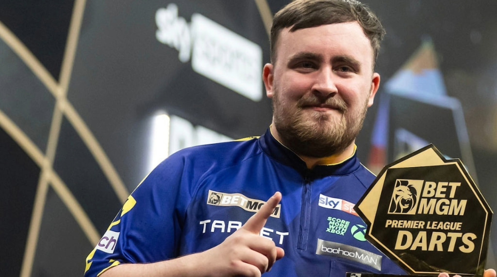 Luke Littler holds aloft one of his Premier League trophies.