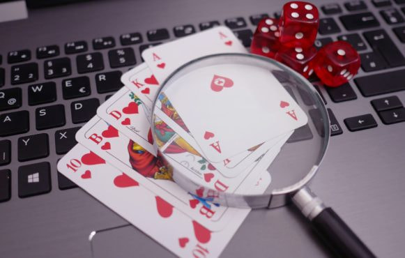 Playing cards, dice, and a magnifying glass, placed upon a laptop to symbolise an analysis of online casino trends.