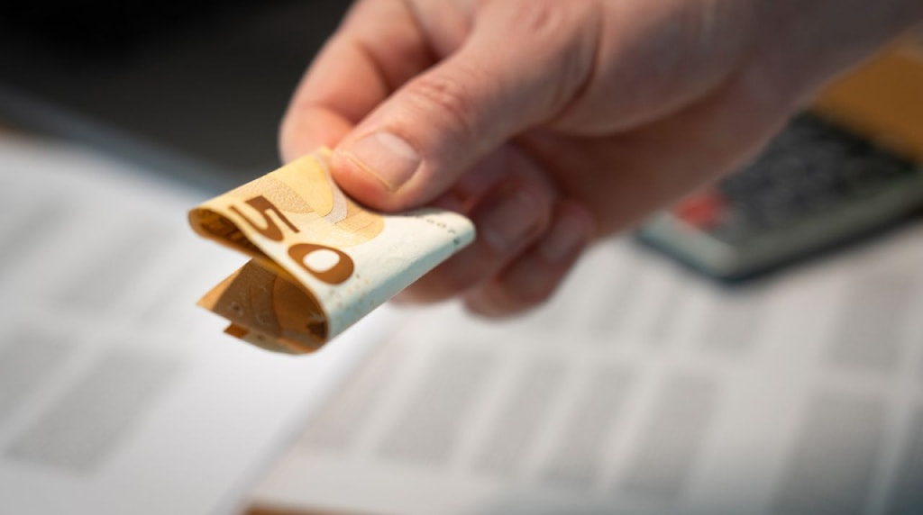 Mannenhand die een opgevouwen briefje van 50 euro geeft