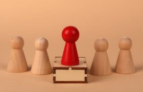 Vijf pionnen, één rode staat middenin op een mini-podium
