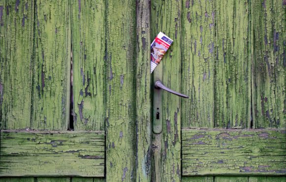 Vecchia porta verde in legno scrostato con volantino nella fessura