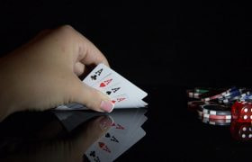 Una mano scopre quattro assi, vicino a fiches e un dado