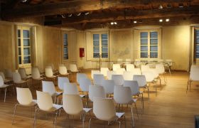 Sala conferenze vuota con sedie bianche e travi a vista.