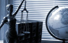 Statua della giustizia accanto a un mappamondo e libri legali.