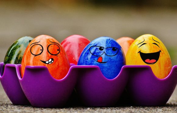Uova di Pasqua colorate con facce sorridenti in portauova viola.