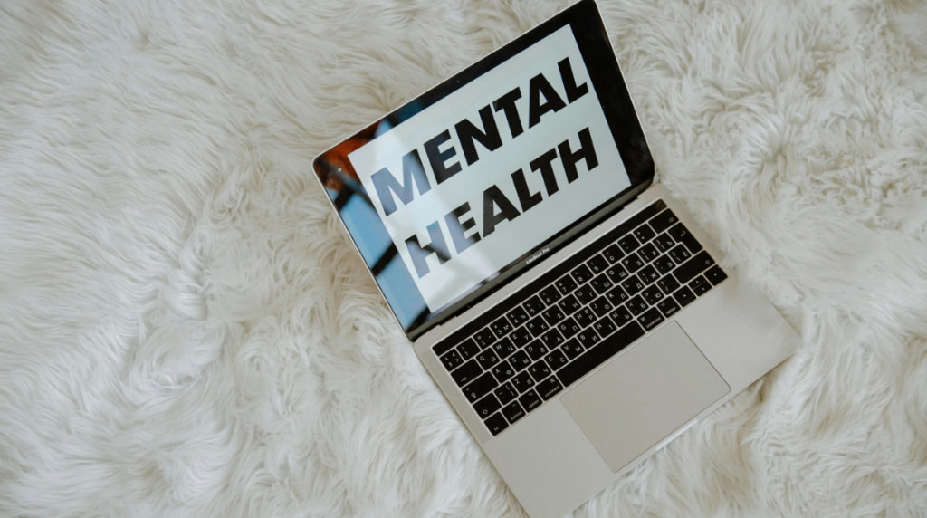 Laptop op wit wollig kleed en op het scherm staat in zwarte letters de tekst “mental health”