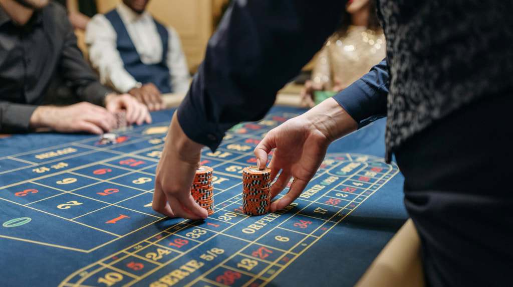 Blauwe roulettetafel waaraan meerdere personen zitten (gezichten zijn niet zichtbaar). Een croupier verplaatst twee stapels fiches.