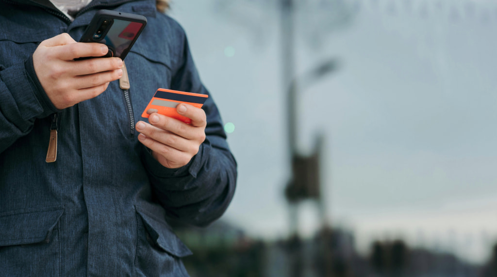 Jongeman met in de ene hand zijn smartphone en in de andere zijn betaalpas