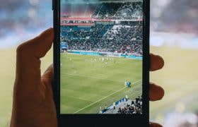 Iemand die in een stadion een voetbalwedstrijd volgt via zijn smartphone