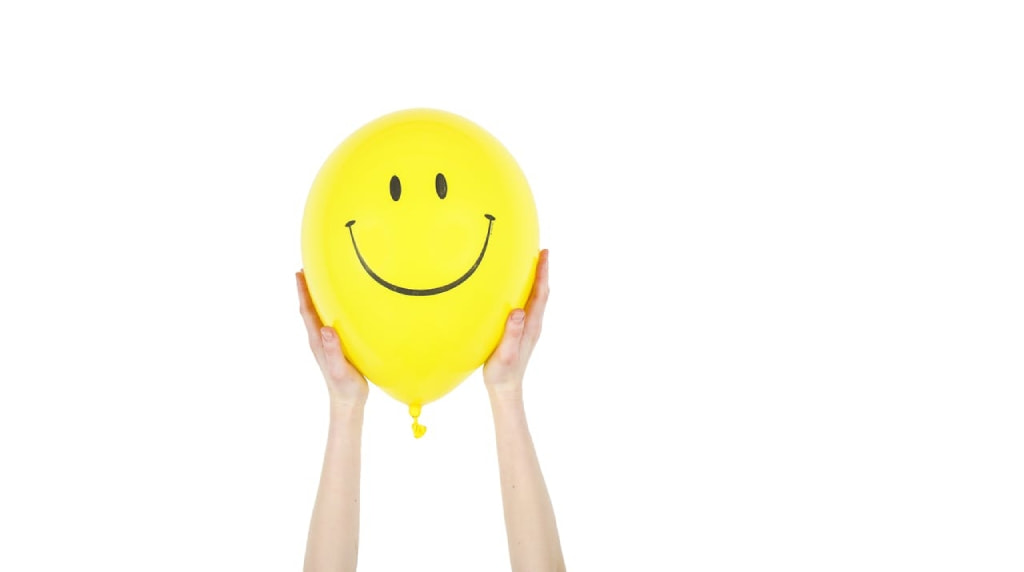 Handen die een gele ballon met lachende smiley vasthouden