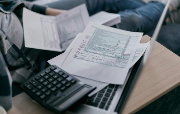 Man op bank met papieren, een rekenmachine en laptop