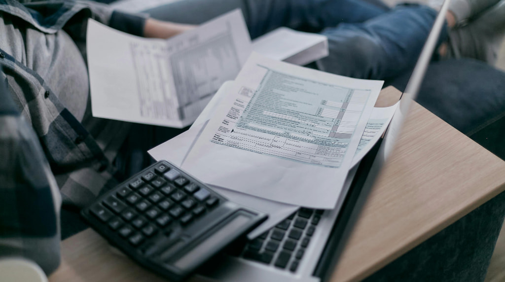 Man op bank met papieren, een rekenmachine en laptop