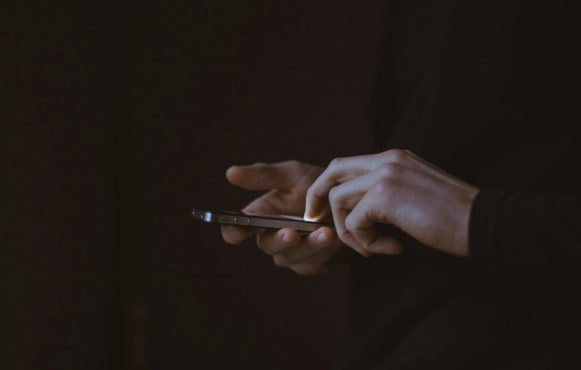 Handen die een smartphone vasthouden, donkere sfeer en achtergrond