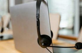 Achterkant van een laptop, waar een zwarte headset aan hangt