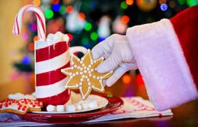 Mâna lui Moș Crăciun ridicând o turtă dulce lângă o cană festivă cu bețe de zahăr
