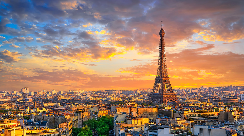 Eiffel Tower overlooking Paris at sunset, with warm clouds and city buildings below.